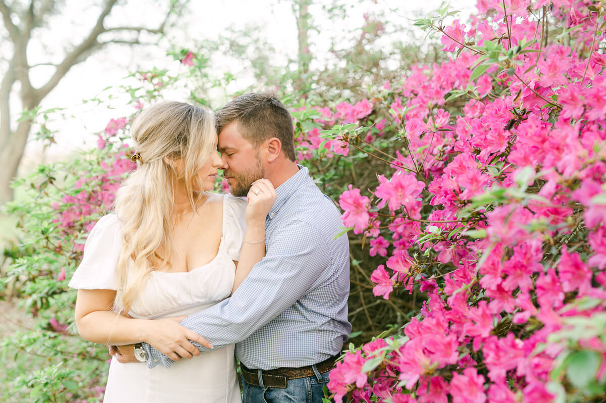 a couple cuddling in front of pink flowers