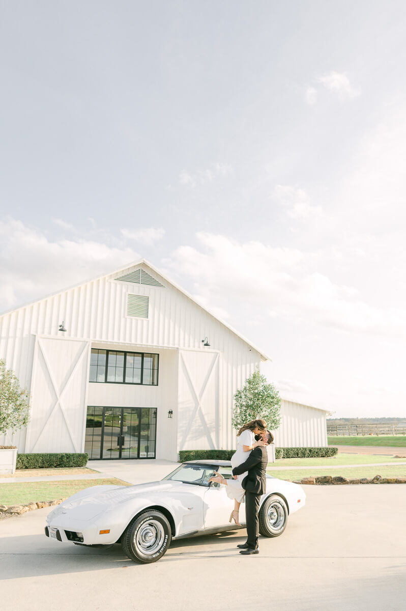 couple in front of the farmhouse wedding venue with vintage car