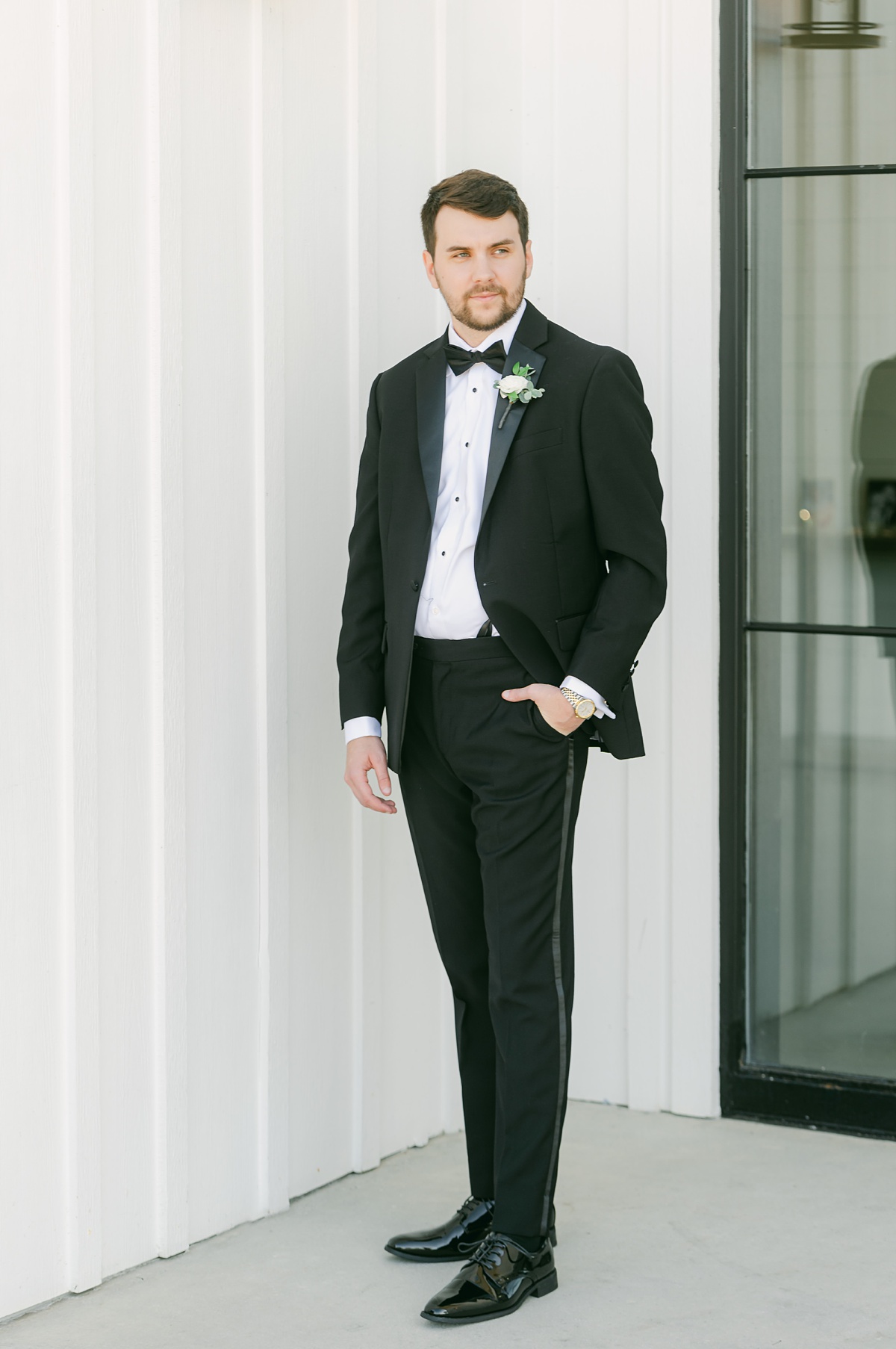 groom wearing classic black suit and bowtie in front of the farmhouse