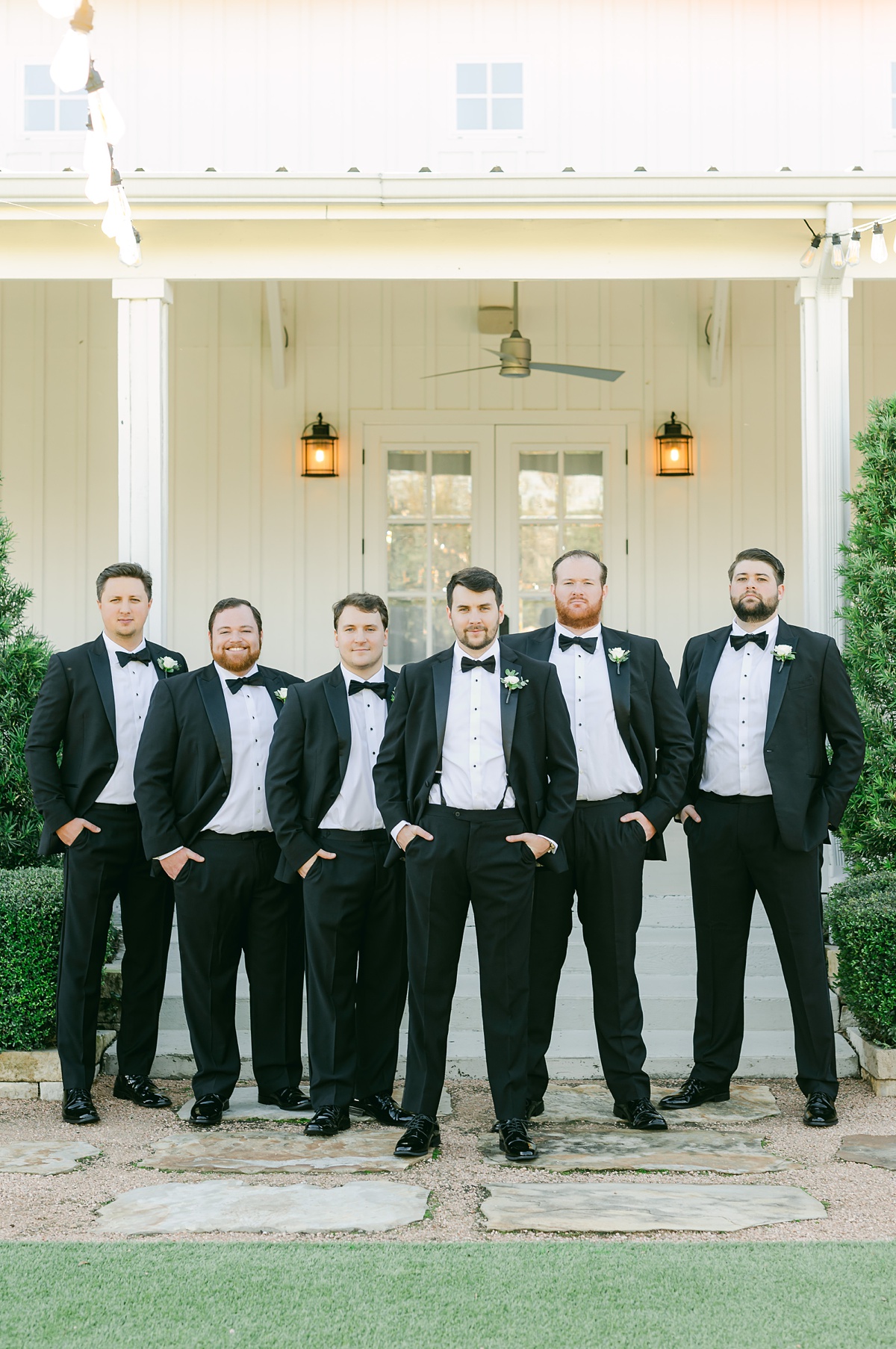 groomsmen wearing black suits posing in front of the farmhouse