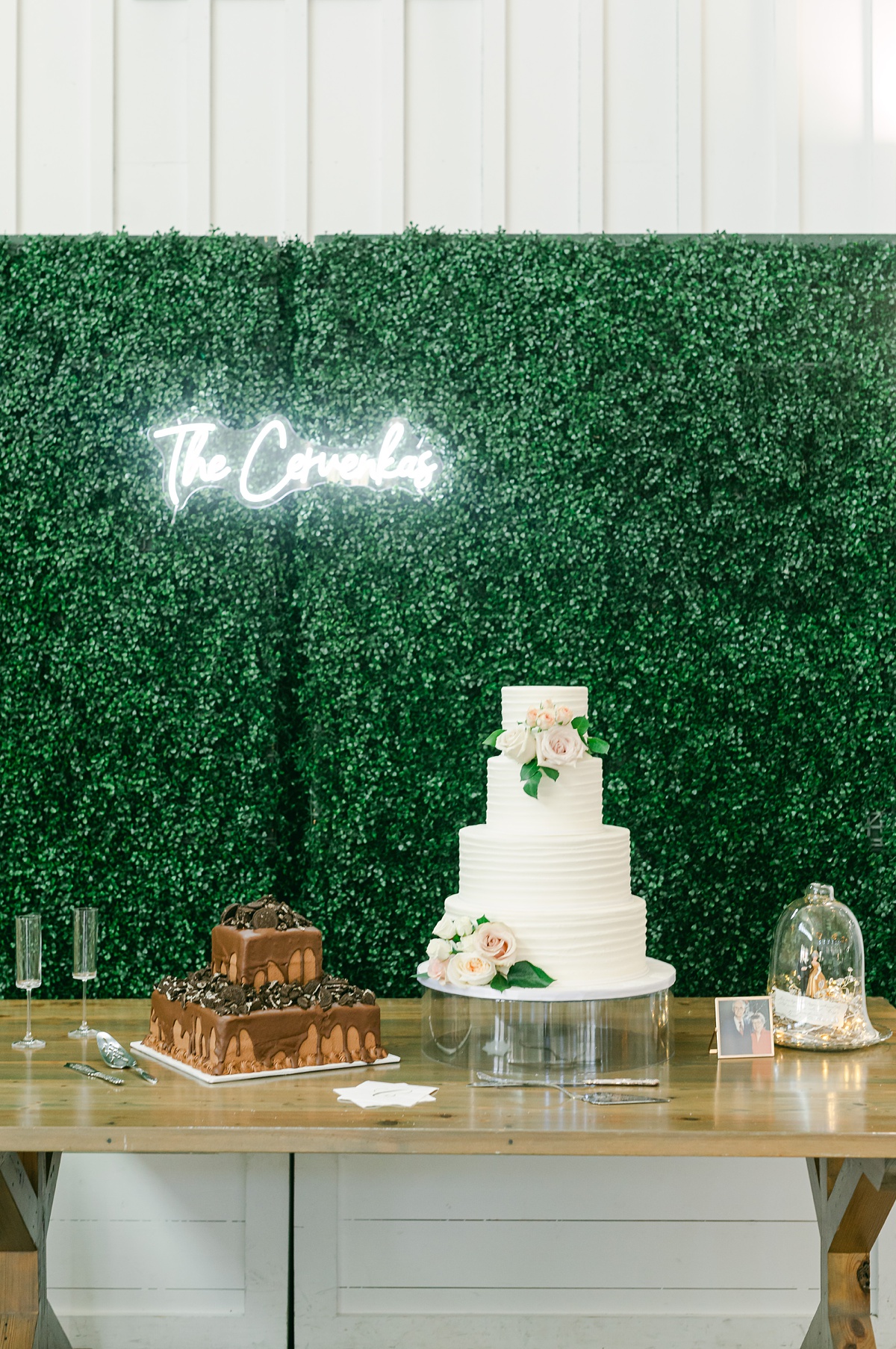 two wedding cakes in front of a greenery wall at the farmhouse