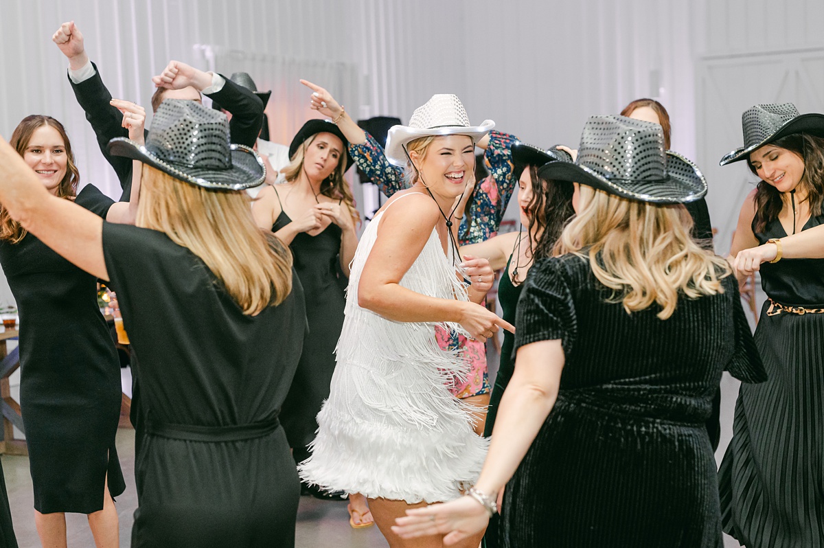 a bride wearing a cowboy hat dancing at her farmhouse wedding
